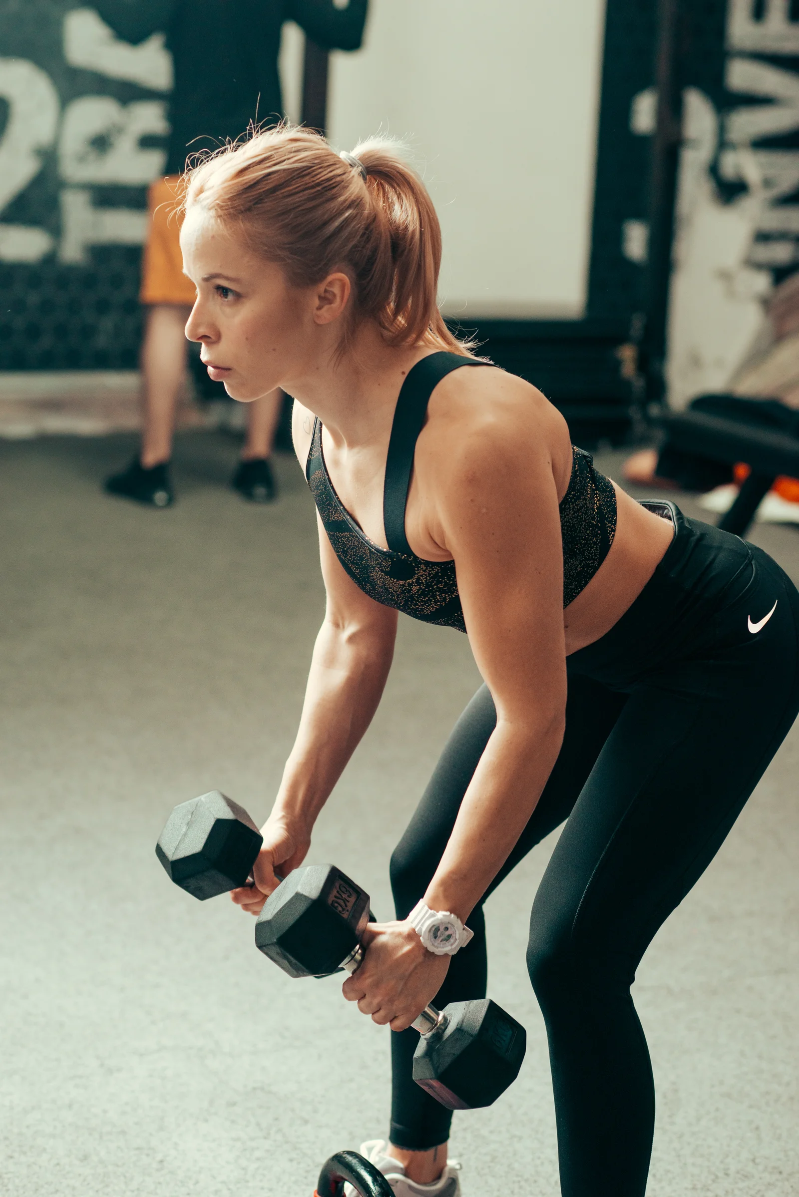 Femme réalisant un exercice de musculation avec des haltères en salle de sport, illustrant l'entraînement en résistance associé à la supplémentation en créatine